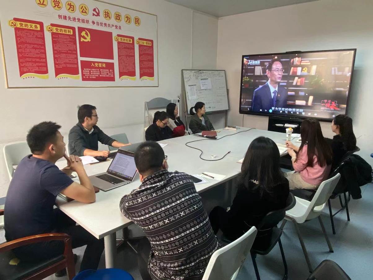 A group of people sitting around a table looking at a screen Description automatically generated with medium confidence